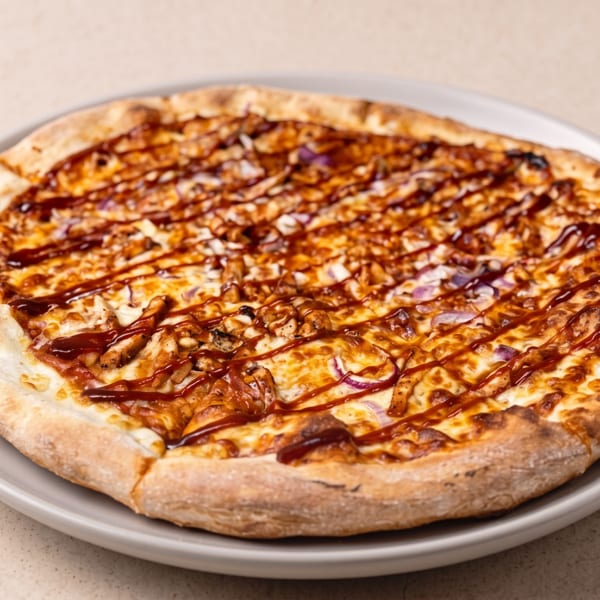 Cheesy pizza topped with mushrooms, red onion, and barbecue sauce drizzle on a gray plate.