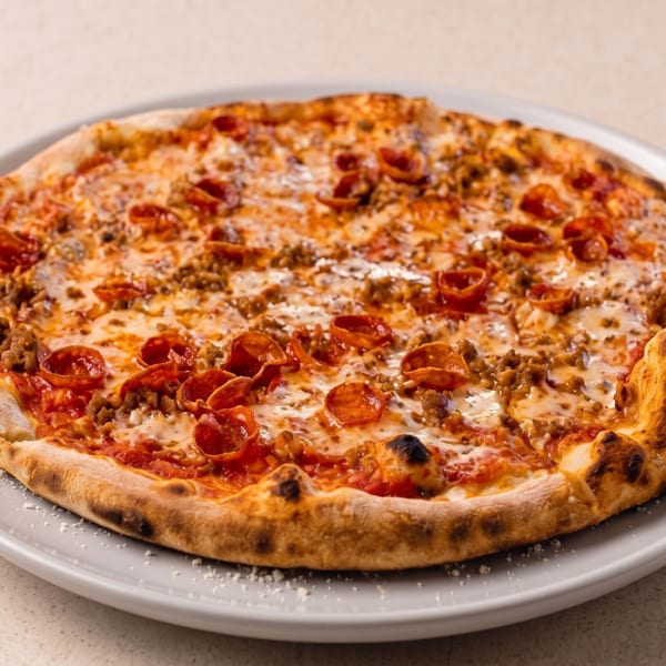 Loaded pepperoni and sausage pizza with melted cheese and charred crust, served on a white plate.