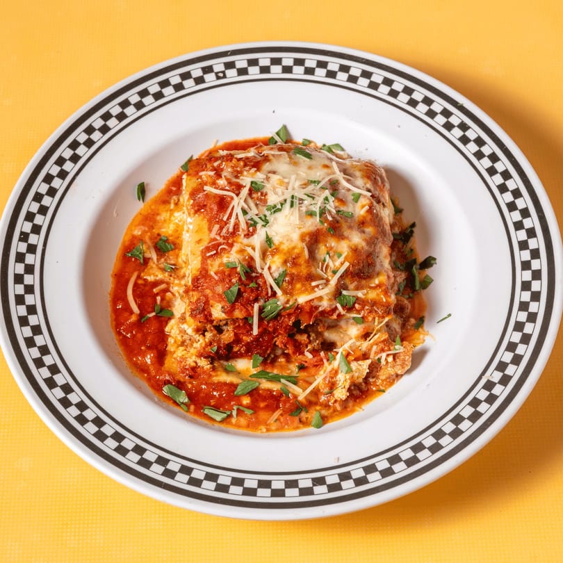A serving of lasagna with melted cheese, red sauce, and fresh parsley on a white plate.
