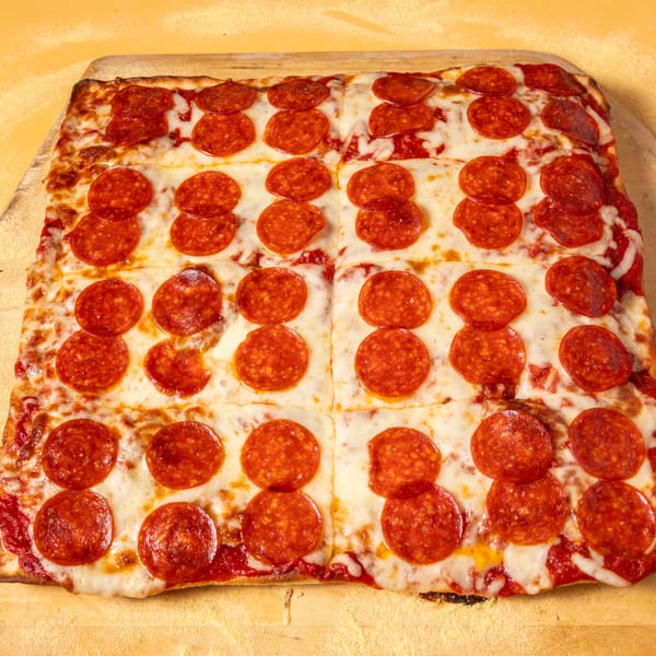 A large rectangular pepperoni pizza, cut into squares, on a wooden pizza peel.