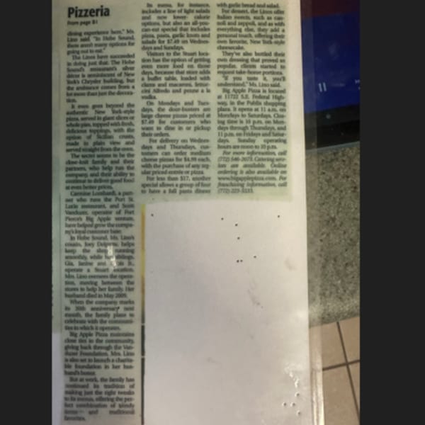 A close-up view of a newspaper article about a pizzeria, with text visible on a white background.
