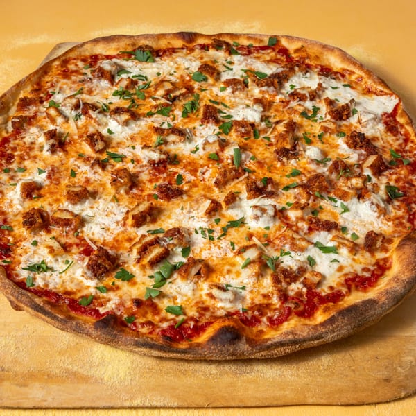 A whole Buffalo chicken pizza with white sauce, red sauce, cheese, and parsley on a wooden peel.