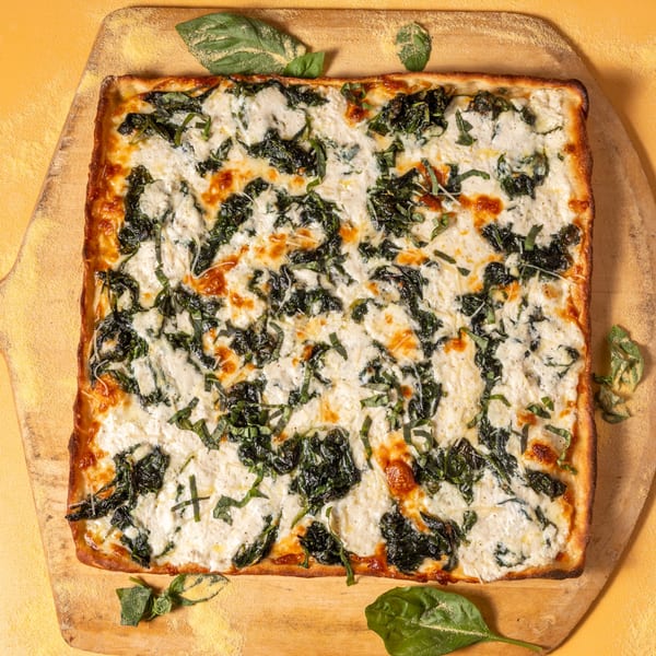 Square white pizza with spinach and basil on a wooden peel.