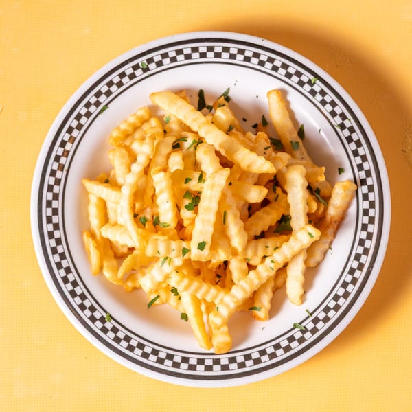 A white plate with a black and white checkered rim holds a pile of golden crinkle-cut fries.